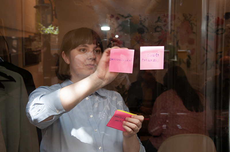 Elina-ja-Post-it-laput-ovessa Nuori nainen laittaa post-it -lappuja toimiston lasioveen vastuullisuusvalmennuksessa.